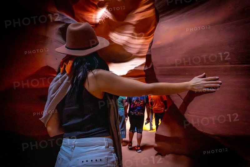 Woman traveler wearing a hat, touching the smooth, winding sandstone walls of antelope canyon while exploring the unique geological formations and colors of the slot canyon