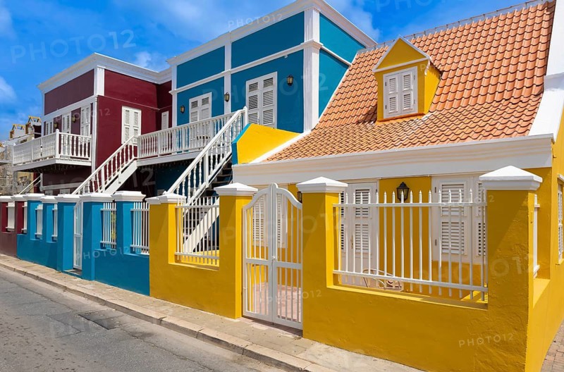 Scenic view of vibrant yellow and blue colonial buildings with white fences in the historic Pietermaai district of Willemstad Curacao under a clear blue sky