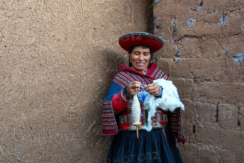 Friendly smiling woman, Valentina in traditional clothes of the Quechua indigenous ethnic group spinning wool with a wooden spindle, traditional crafts, Urubamba Valley, southern Peru, Peru, South America