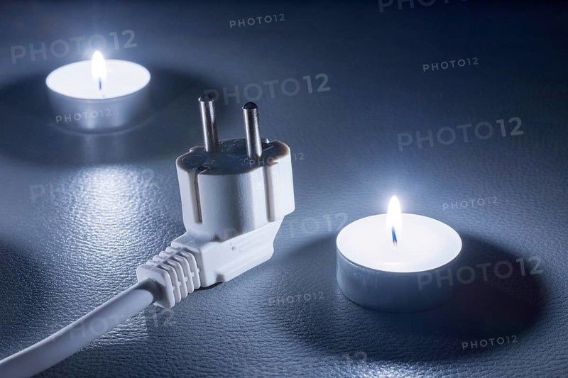 Two candles and an electric cable in cold light on a dark background, symbolic picture, power failure, blackout, plug