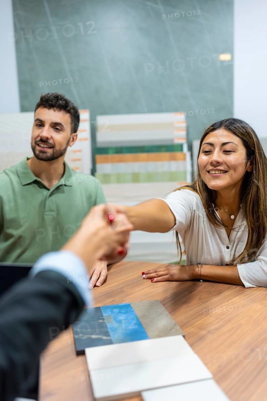 Happy couple concluding a deal and shaking hands with a sales agent over a table with tile samples, symbolizing a new home renovation project and successful collaboration in a showroom