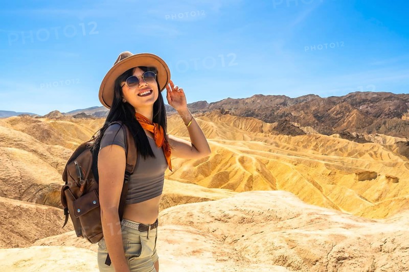 Young woman smiling while exploring the unique badlands landscape and enjoying the panoramic desert scenery under a clear blue sky at death valley national park