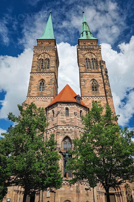 Front view of St Sebaldus Church in Nuremberg, Germany, with twin church towers, red roof detail and trees below