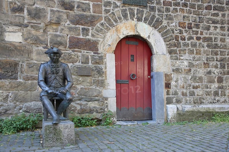 Penn Soldier sculpture by Klaus Gehlen 2007, historic soldier in uniform on red wooden door with fittings, sitting, guard, guard, modern art, bronze sculpture, life-size, pennsoldier, city history, marching gate, old town, Aachen, Eifel, North Rhine-Westphalia, Germany