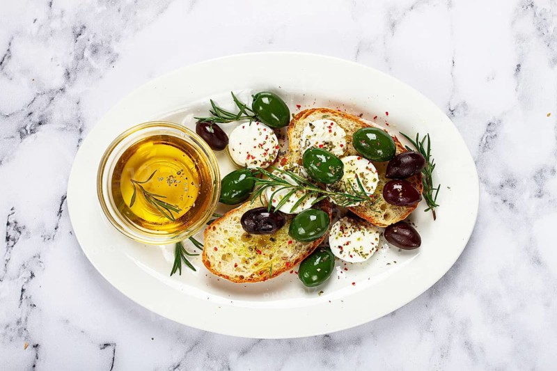 A plate with a snack, ciabatta bread with cheese and olives, olive oil, spices and herbs, top view, no people