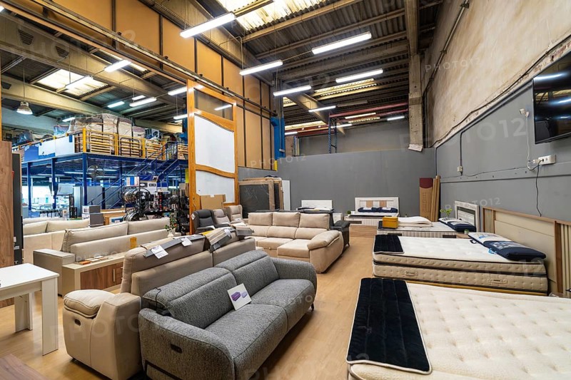 Large interior view of a furniture showroom and retail store. Offering a wide selection of sofas. Mattresses. And beds. With merchandise displayed for a comfortable home furnishing shopping experience