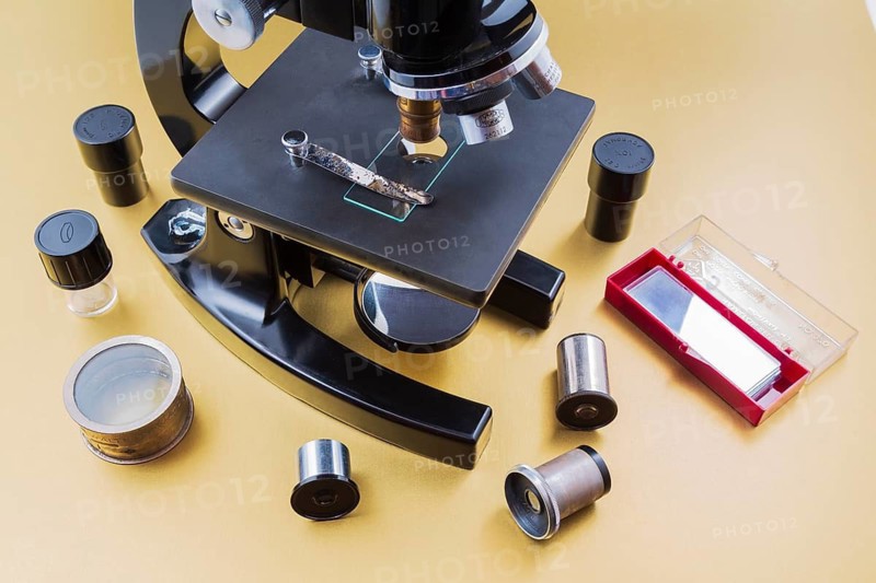 Vintage black Bausch & Lomb research microscope with box of glass slides and objectives on light golden paper background, Studio Composition, Quebec, Canada