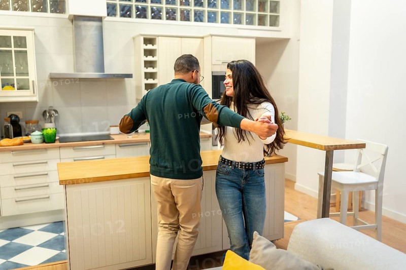 Cheerful couple holding hands while dancing playfully in a modern home kitchen, sharing a romantic and intimate moment together focusing on love, happiness, and joyful domestic lifestyle