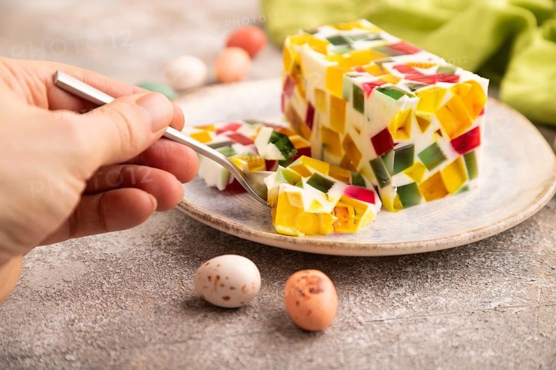 Colored Fruit and milk jelly with hand on brown concrete background and green linen textile, side view, close up, minimalism, selective focus