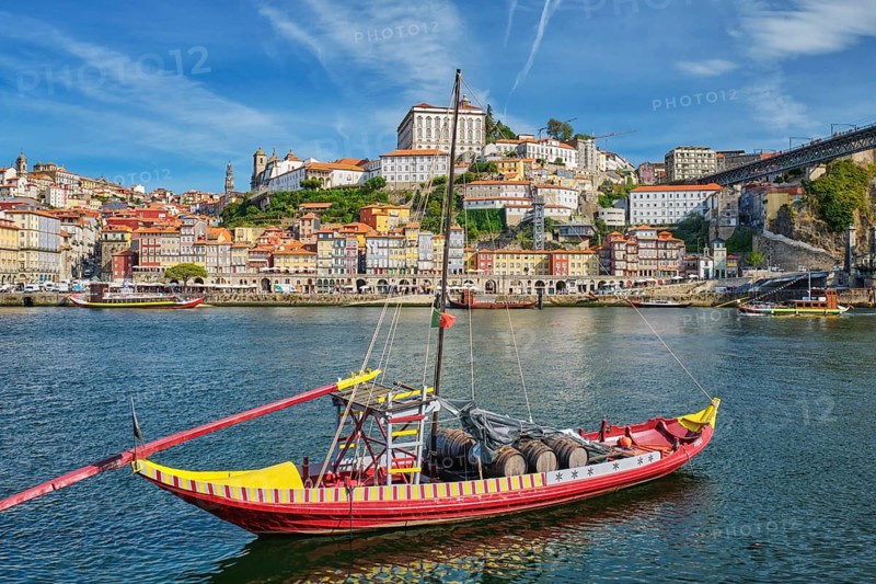 Rabelo boat on the Douro River by Porto Ribeira, Portugal, with wide riverfront skyline and wine barrels near Vila Nova de Gaia