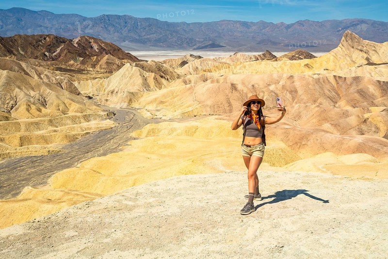 Happy young woman adventurer enjoying desert landscape at zabriskie point in death valley national park, capturing travel memories with a smartphone selfie