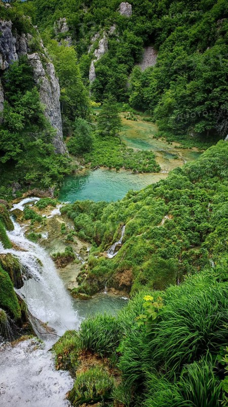 Waterfall flows into a clear lake surrounded by lush nature, Plitvice Lakes National Park, Croatia