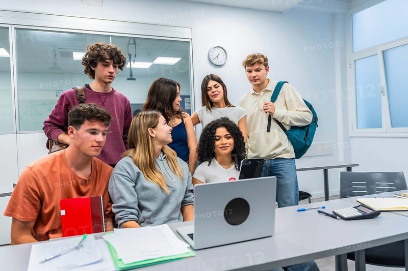 Diverse group of college students collaborating around a laptop in a bright classroom, studying together, brainstorming and using technology for teamwork and skill development