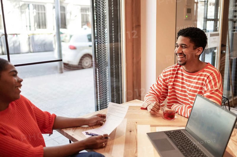 Two colleagues engage in a lively discussion at a coworking space, enhancing productivity. A laptop and documents are on the table, reflecting a modern, collaborative work environment
