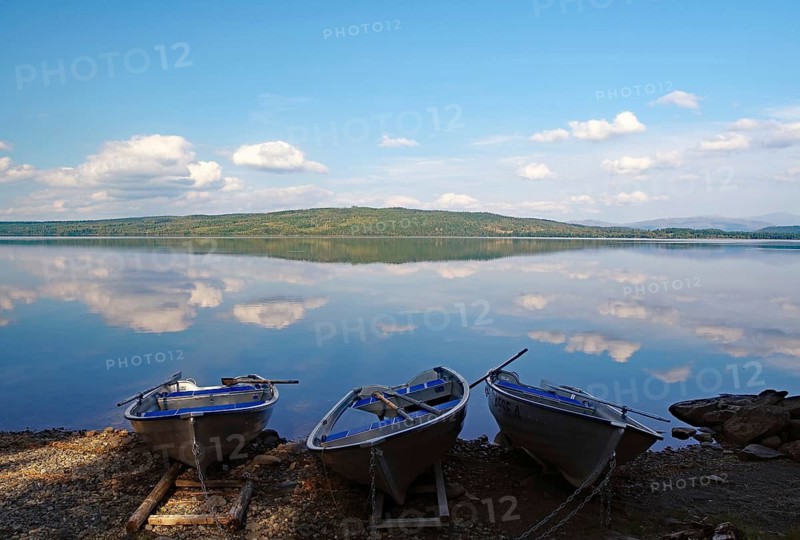 Three calm boats on the shore of a mirror-like lake under a blue sky, Störlien, Jämtland, Sweden