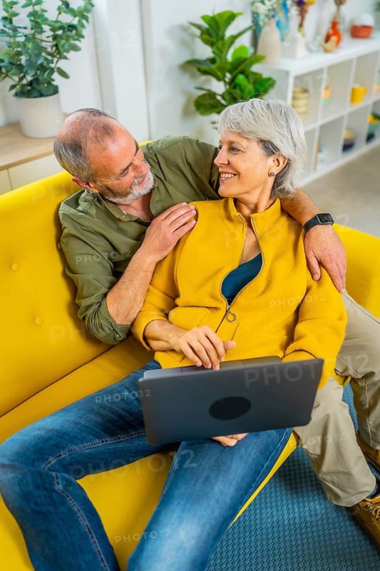 Vertical top view of a modern senior couple using laptop relaxed on the sofa together