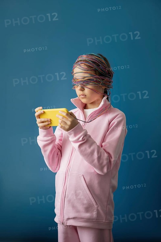 A child stands absorbed in a smartphone, eyes covered by tangled colorful wires, symbolizing the complex and potentially overwhelming influence of the internet on young minds