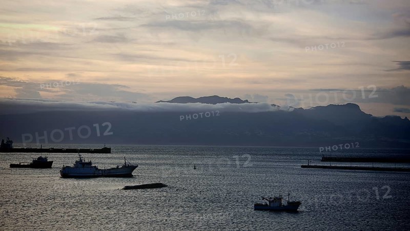 Boats on calm seas in front of a mountain range and cloudy sky at dusk, mountains of Santo Antao in the background, view over Mindelo Harbour, Sao Vicente, Cabo Verde, Cape Verde, Cape Verde