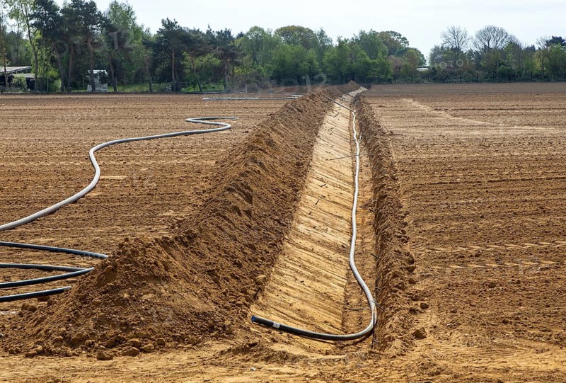 Poly pipe subsurface irrigation system in excavated ditch across sandy field, Shottosham, Suffolk, England, UK