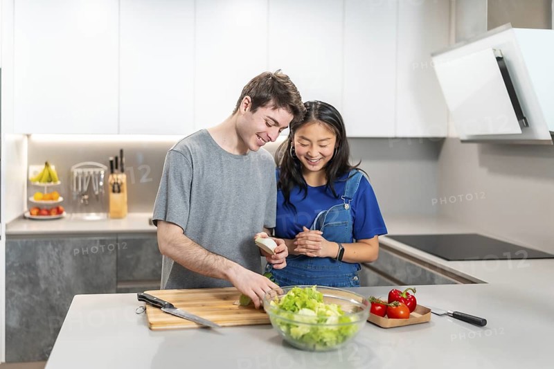 Happy multiethnic couple preparing a fresh salad together in their modern kitchen, enjoying quality time and healthy eating habits