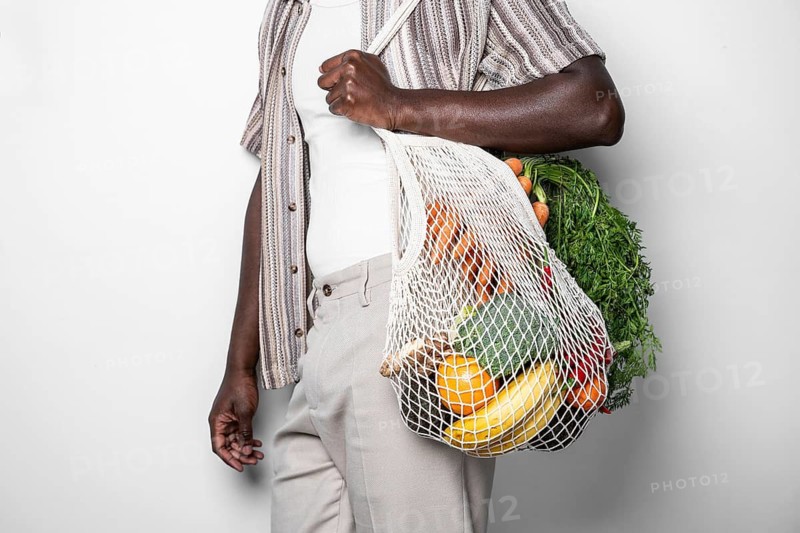 A close-up image of a man holding a reusable mesh bag filled with various fresh vegetables and fruits, showcasing sustainable shopping and eco-friendly lifestyle choices
