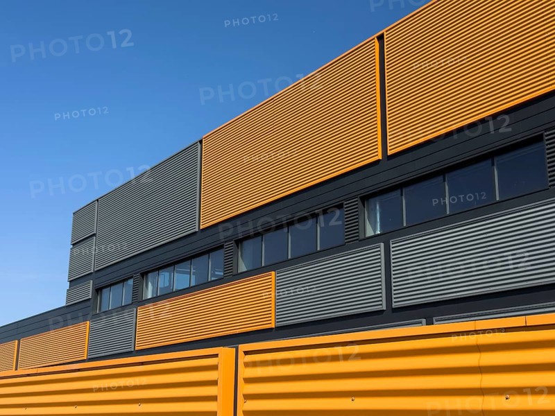 A striking modern industrial building featuring vibrant yellow panels juxtaposed with gray elements under a clear blue sky