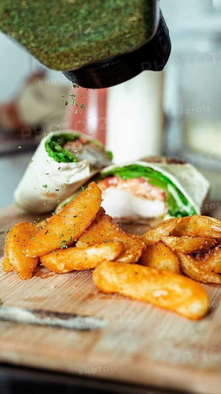 A close-up of crispy fried potato wedges garnished with herbs alongside a fresh chicken wrap, set in a cafe ambiance. Perfect for food and culinary themes