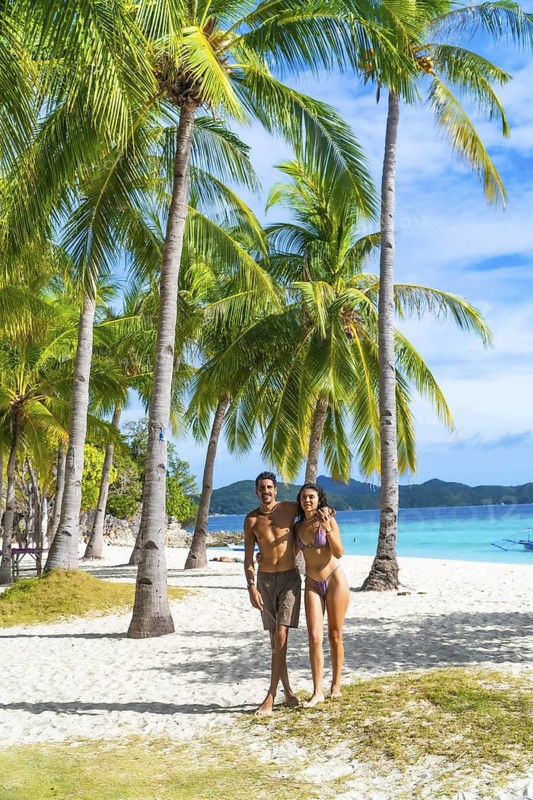 Tourists enjoying their holidays on a beautiful white sand beach surrounded by palm trees on malcapuya island, coron, philippines