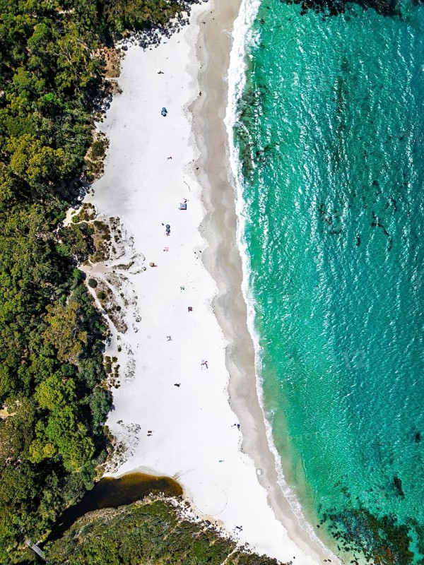 A breathtaking aerial view showcases a pristine beach with crystal clear turquoise waters, soft white sand, and lush greenery, presenting a tranquil coastal paradise in Jervis Bay, Australia