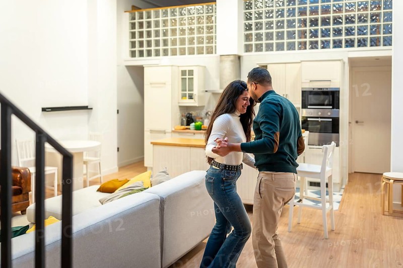Happy young couple dancing and smiling in a bright contemporary apartment, sharing a cozy, spontaneous moment of romance, connection and domestic joy