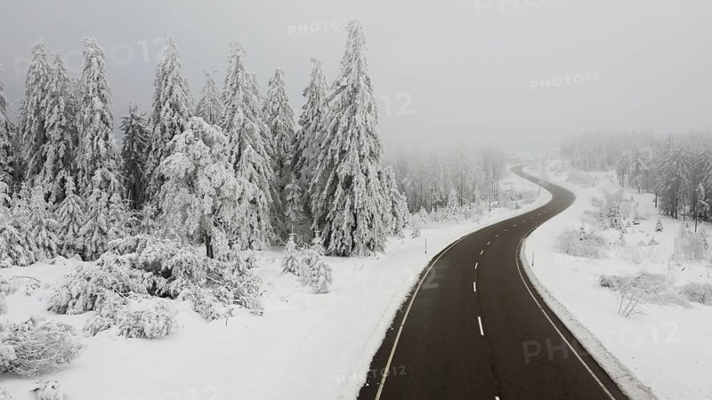 Snowy road leading through foggy winter landscape with snow-covered trees, aerial view, road with snow in winter, Black Forest, Germany
