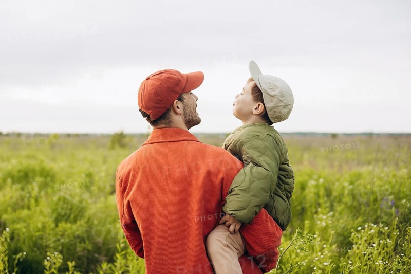 A father and his young son enjoy a serene walk through a lush green field, creating cherished memories on a sunny day. The landscape provides a perfect backdrop to their bonding moment