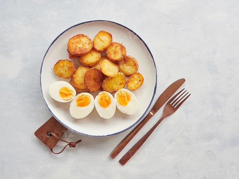 Crispy golden brown roasted potatoes sliced and hard boiled egg halves plate, knife and fork on the table