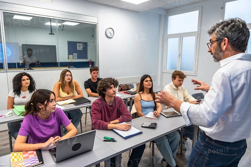 Professor giving an engaging university lecture to attentive students in a modern classroom, taking notes and using laptops and tablets during interactive group learning and discussion