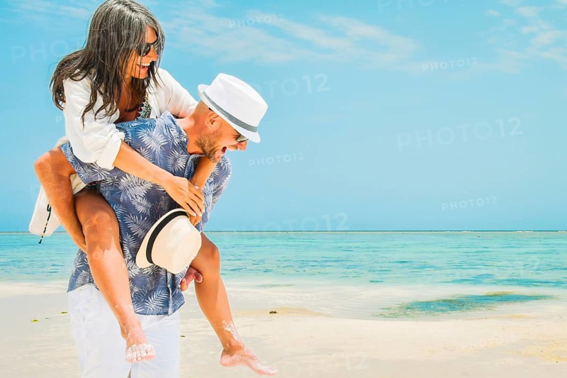 Cheerful young man giving woman piggyback ride walking along turquoise ocean shoreline sandy beach Zanzibar tropical island resort destination sunny summer day