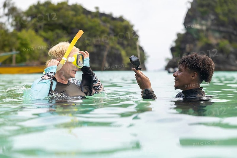 Tourist and guide enjoy snorkeling in the crystal-clear waters of Raja Ampat, West Papua, surrounded by lush green cliffs They share a moment of joy and a deep appreciation for nature