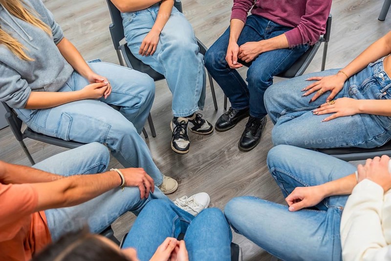 People are sitting in a close circle, creating a sense of unity and shared experience, fostering mental health support and open communication within a community group setting