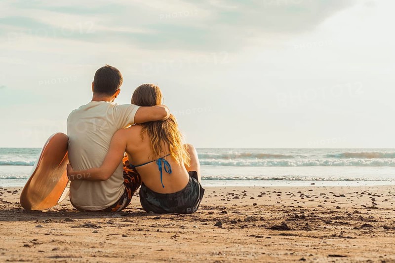 Caring gesture captured in natural light as the couple gazes toward the horizon, evoking feelings of comfort, trust and summer freedom on a quiet and beautiful coastline