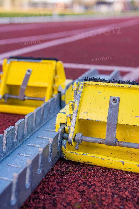 Two yellow starting blocks on a red track, ready for a race