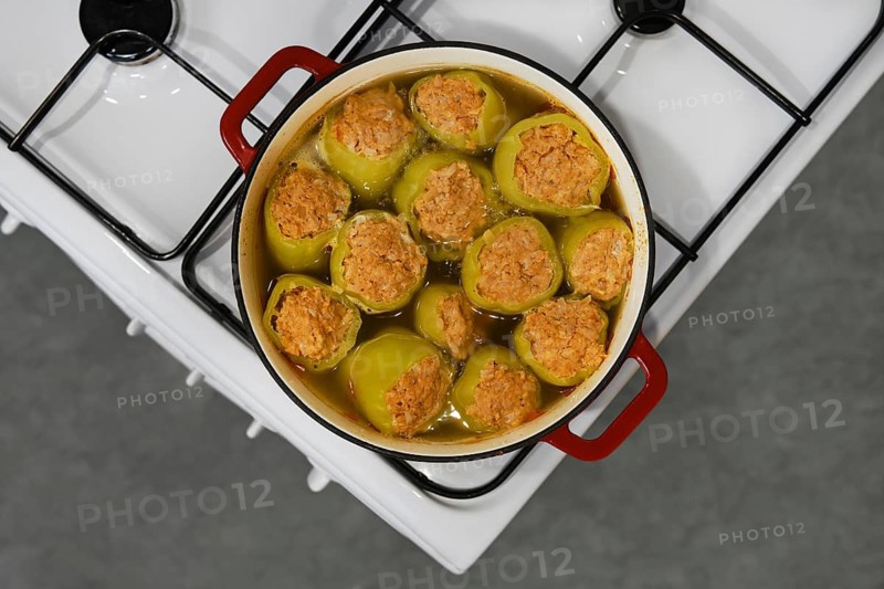 Bell peppers stuffed with minced lamb meat are cooked in cast iron pot on stove, top view