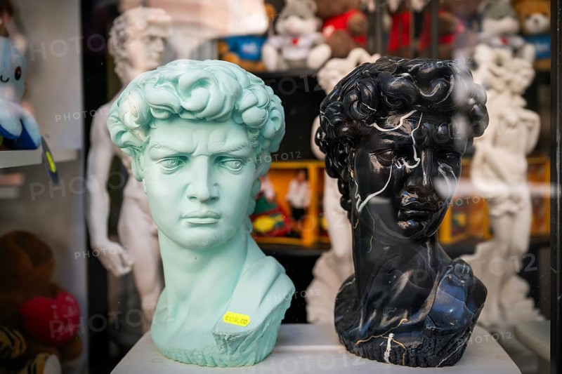 A turquoise and a black bust depicting Michelangelo's David stand in the display case of a souvenir shop, old town, Florence, Tuscany, Italy
