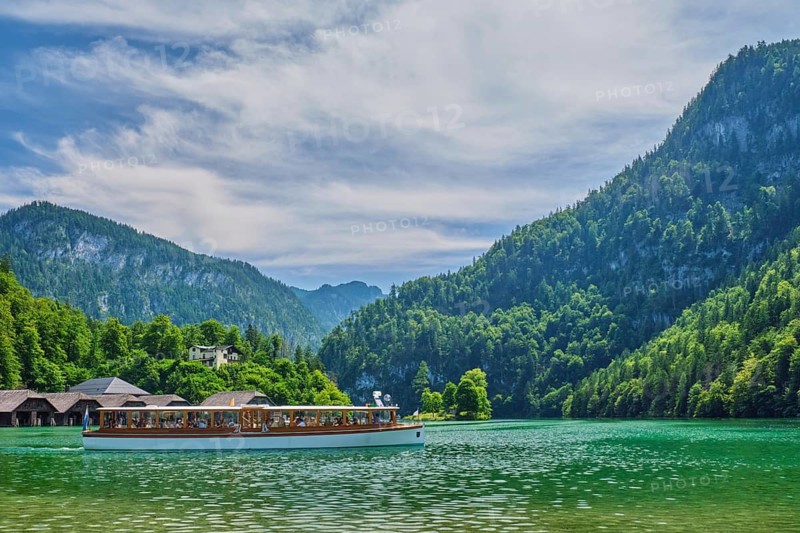 Side view of a white electric passenger boat cruising the emerald Konigsee lake under a dramatic sky in Berchtesgaden National Park, Bavaria, Germany