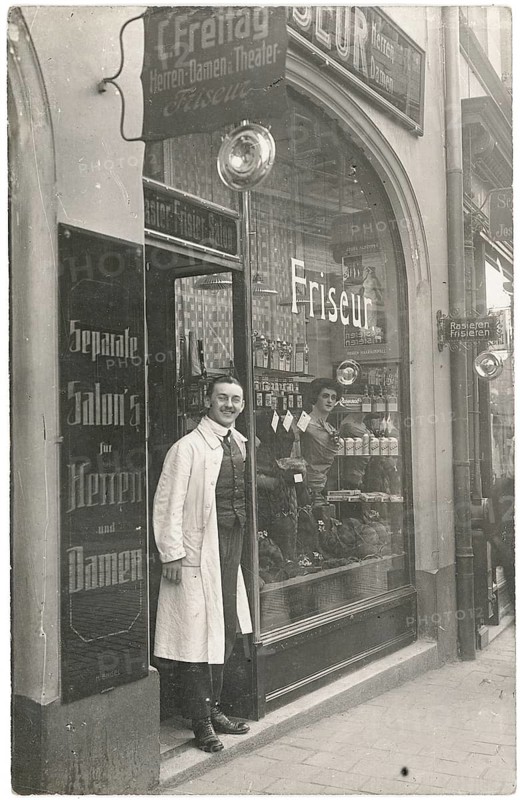 Hairdresser, shop, profession, twenties, hairdresser in traditional clothes stands at the door of a hairdressing salon in a historic setting, around 1920