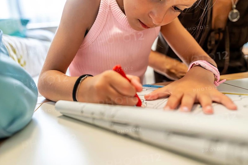 Young girl coloring a drawing on paper, sitting at a table with her grandmother, engaging in educational activities and developing her creativity in a cozy indoor setting