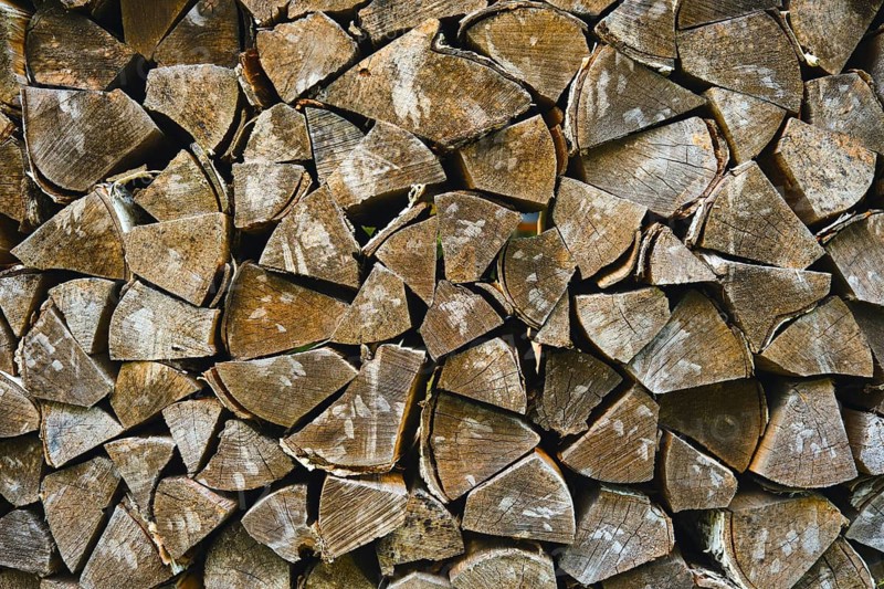 Wood logs arranged neatly for use in heating homes during winter months in rural location. Logs show signs of aging and are cut into various sizes for easy storage and access