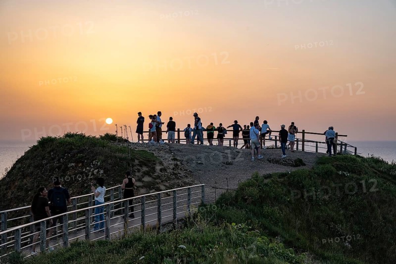 Tourists stand on the observation deck of the Falaise d'Aval rock formation and tourist attraction near Étretat and watch the sunset over the English Channel, Alabaster Coast, La Côte d'Albâtre, Chalk Cliffs, Seine-Maritime, Normandy, France