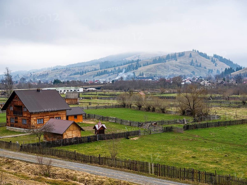 Wooden house with fenced meadows, hills in fog behind, Moldova, Romania