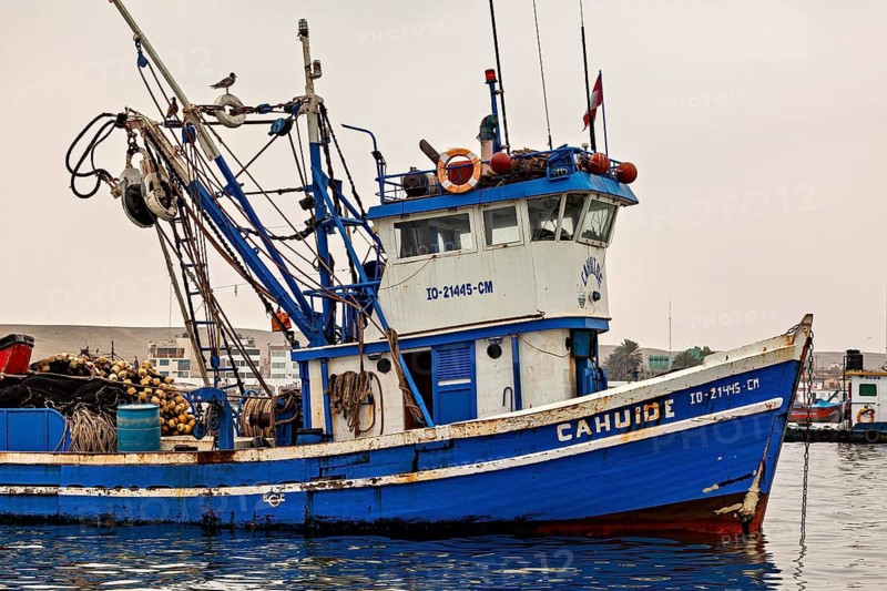 Close-up of a blue fishing boat with nets and ropes, in front of a harbor, fishing trawler in the port of Paracas in Peru