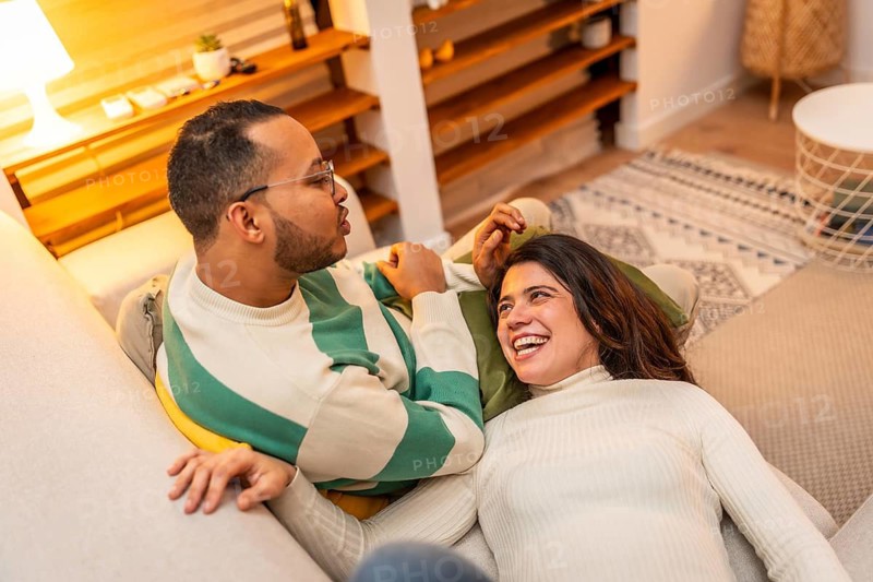 Happy young couple enjoying a comfortable moment on the sofa, finding joy and connection in shared conversation and laughter during an intimate evening alone together in their cozy living room