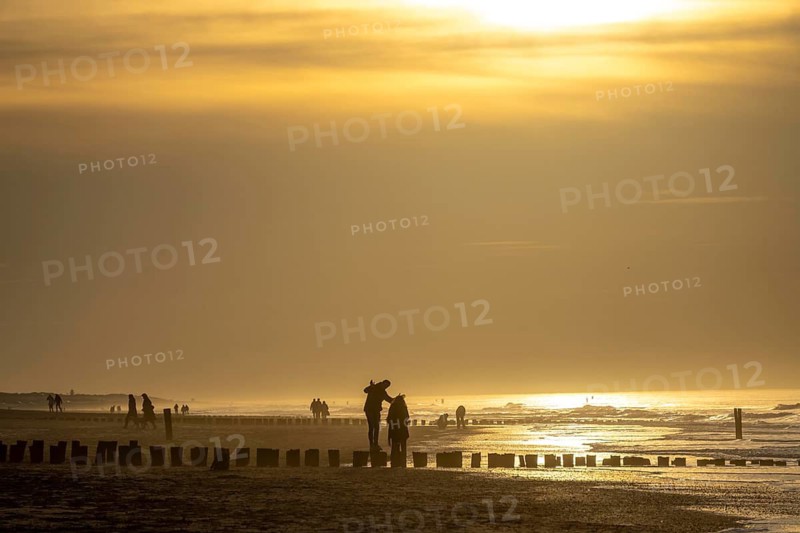Winter on the North Sea, sunset at sea, beach walkers, coastal protection, through wooden posts, paalhoofden, on the beach, breakwater, the piles rammed into the sandy soil in double rows slow down the waves and ocean currents and thus slow down the flow rate of seawater, so less sand is washed away from the standing position, near Domburg, Walcheren peninsula in the Dutch province of Zeeland
